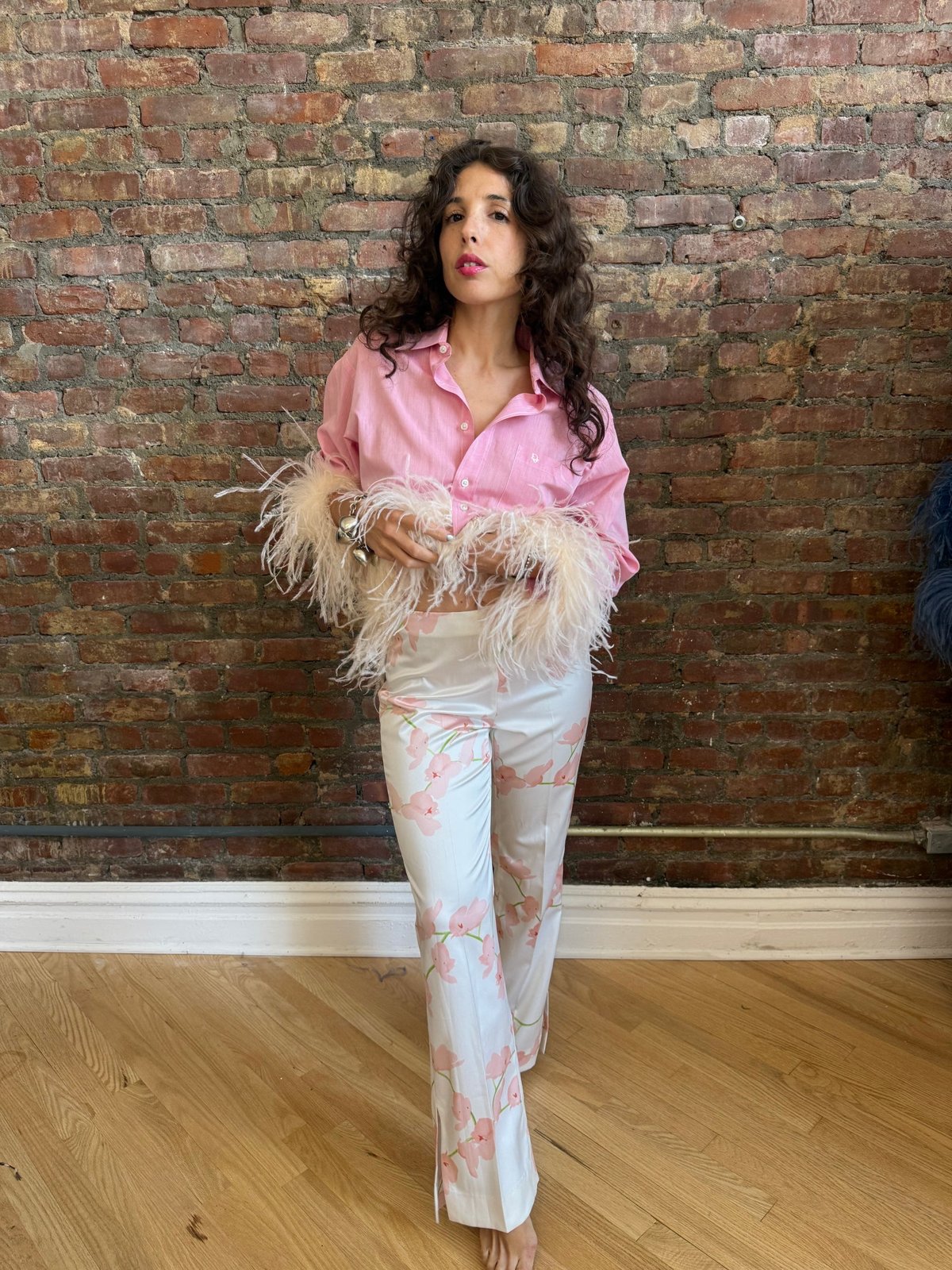 Model wearing a pink button-down shirt with detachable ostrich-feather cuffs and pink floral pants &mdash; one of Amanda&rsquo;s custom upcycles.