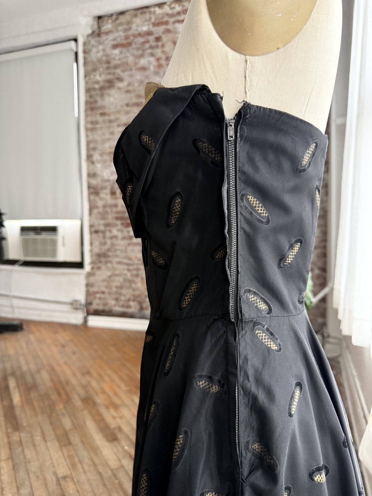 Metal zipper running down the side of a black cocktail dress on a mannequin.