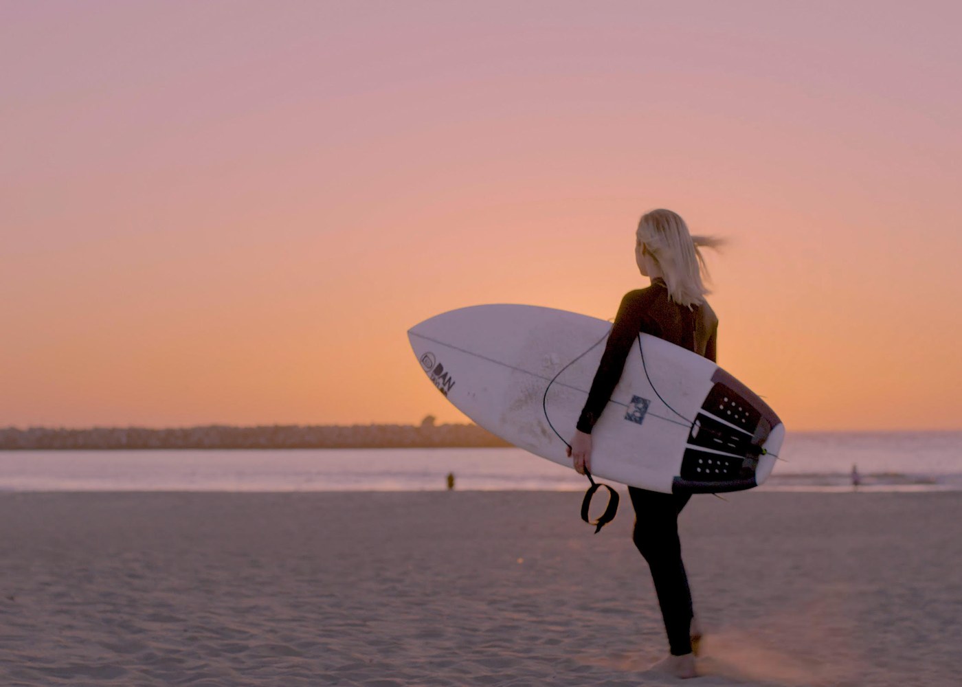 Lindsay McCormick walking on the beach with a surfboard.