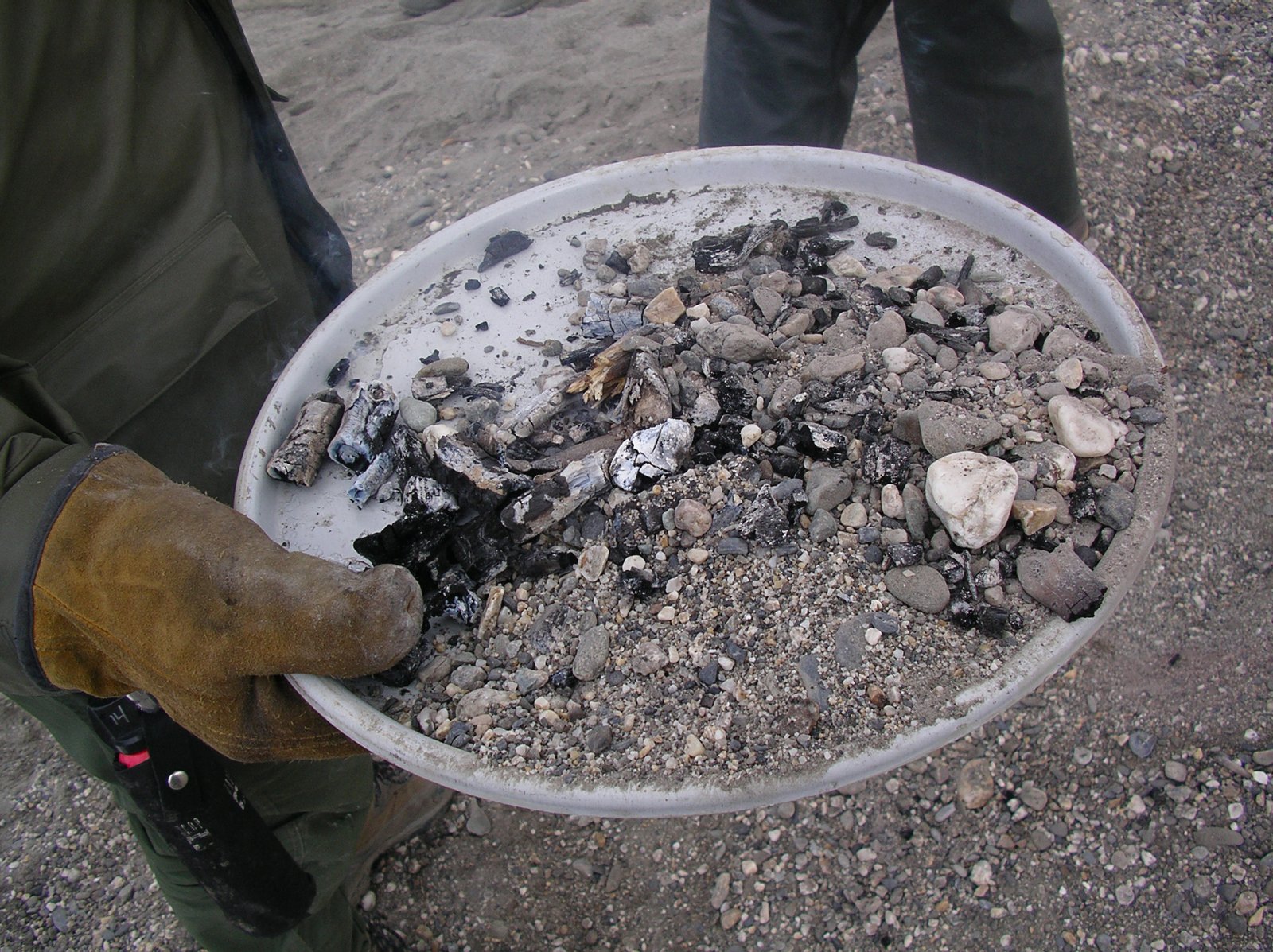 Backcountry campers packing out cold campfire ashes and coals.