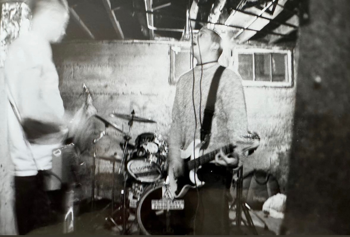 wellspring playing a basement show, guitarist mid-song against a cinderblock wall.